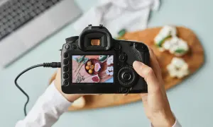 Dłoń trzyma aparat fotograficzny, na którego ekranie widać zdjęcie jedzenia.