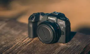 Czarny aparat Canon EOS R z zaślepką na obiektyw na drewnianym stole.