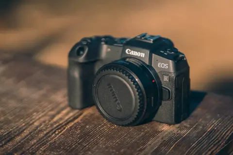 Czarny aparat Canon EOS R z zaślepką na obiektyw na drewnianym stole.
