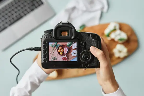 Dłoń trzyma aparat fotograficzny, na którego ekranie widać zdjęcie jedzenia.